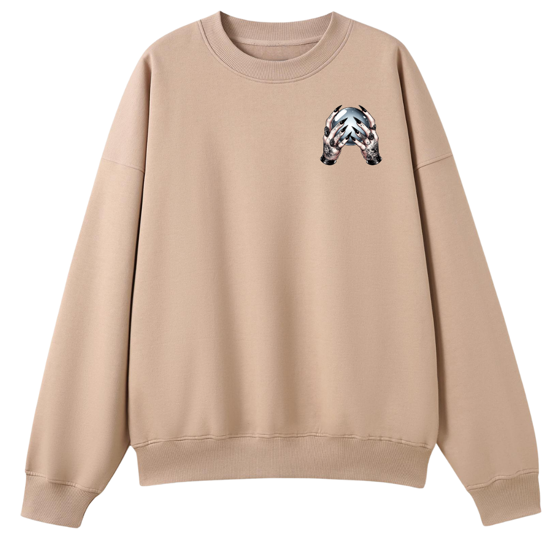 A beige crewneck sweatshirt with a small black, white, and gray patterned graphic on the left chest, displayed on a solid white background.