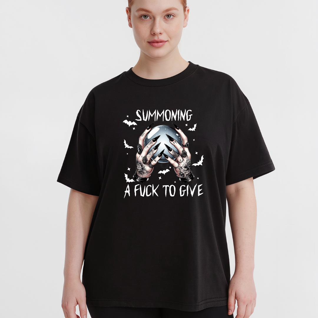 A model wearing a black oversized graphic t-shirt with a white and gray design featuring hands holding a skull and the text 'SUMMONING A FUCK TO GIVE'.