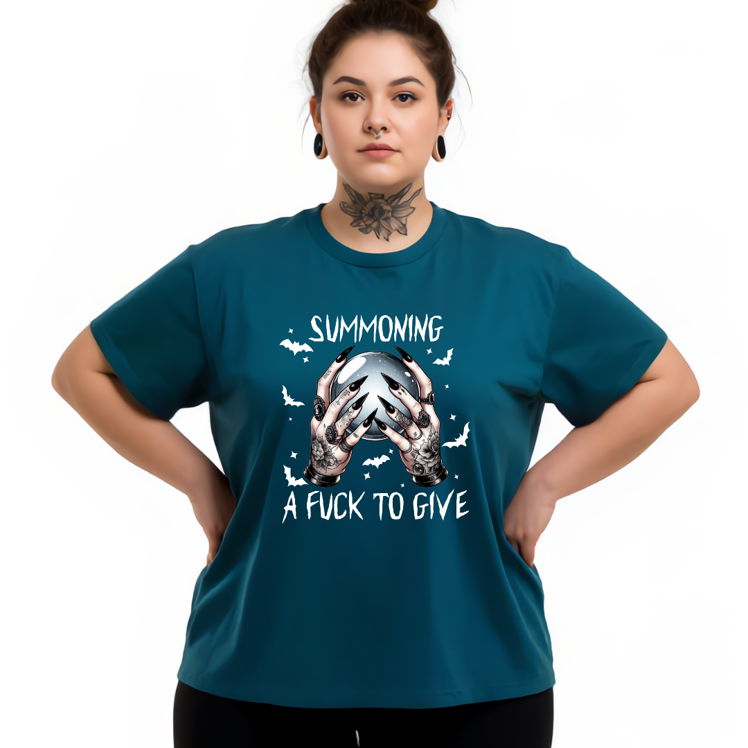 A woman modeling a teal short-sleeve graphic t-shirt with a white and silver design featuring the text 'SUMMONING A FUCK TO GIVE' and a skull illustration, set against a plain white background.