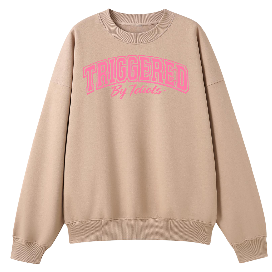 A beige crewneck sweatshirt with a pink graphic text print reading 'TRIGGERED By Teachers' on the chest, displayed against a solid white background.