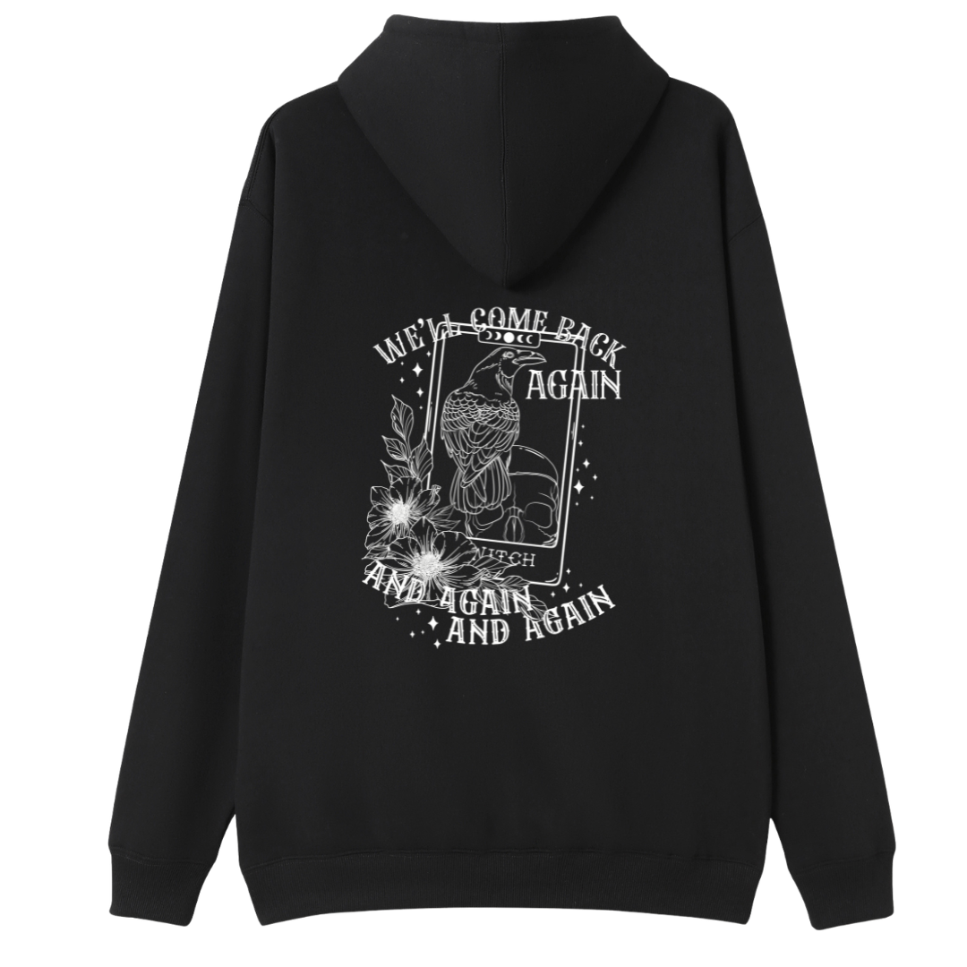 A black oversized hoodie shown from the back, with the We'll Come Back Again graphic printed large across the back, a crow on a tarot card framed by flowers.