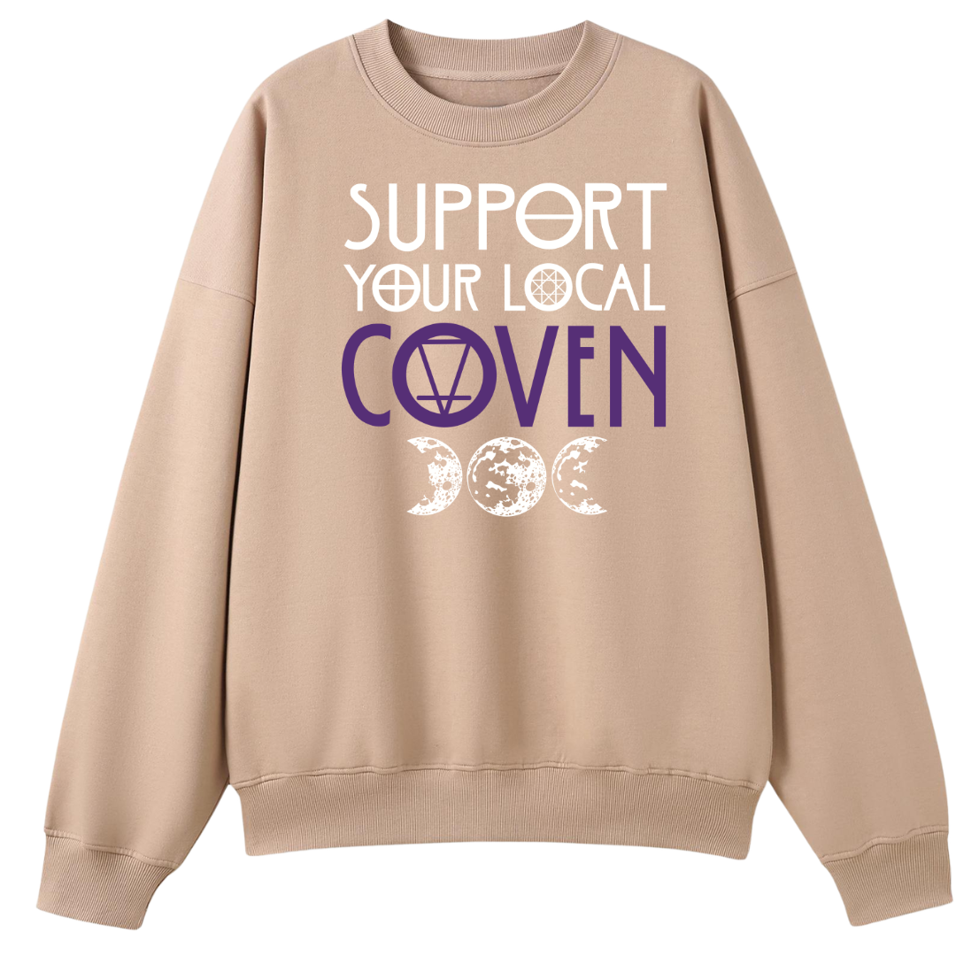 A peach oversized crew neck with the Support Your Local Coven graphic printed large on the front, purple lettering above a triple moon.