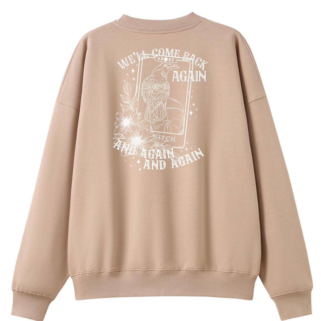 A peach oversized crew neck shown from the back, with the We'll Come Back Again graphic printed large across the back, a crow on a tarot card framed by flowers.