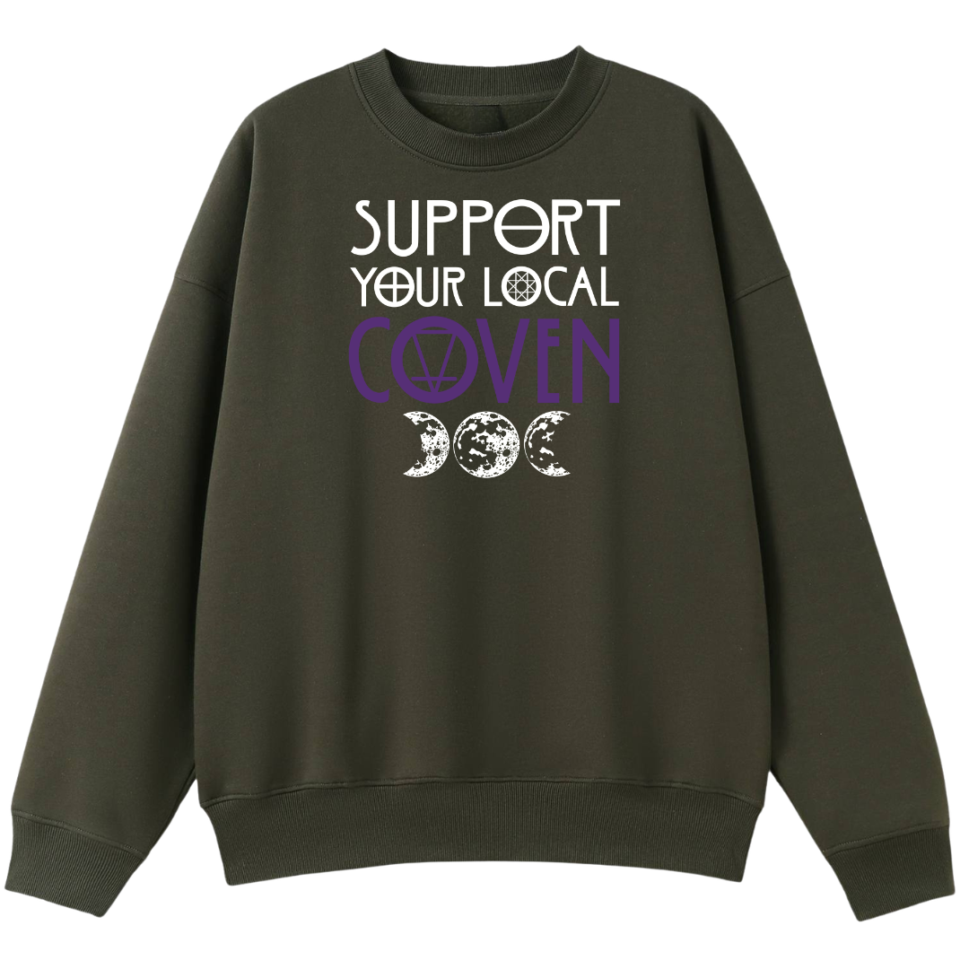 An army green oversized crew neck with the Support Your Local Coven graphic printed large on the front, purple lettering above a triple moon.