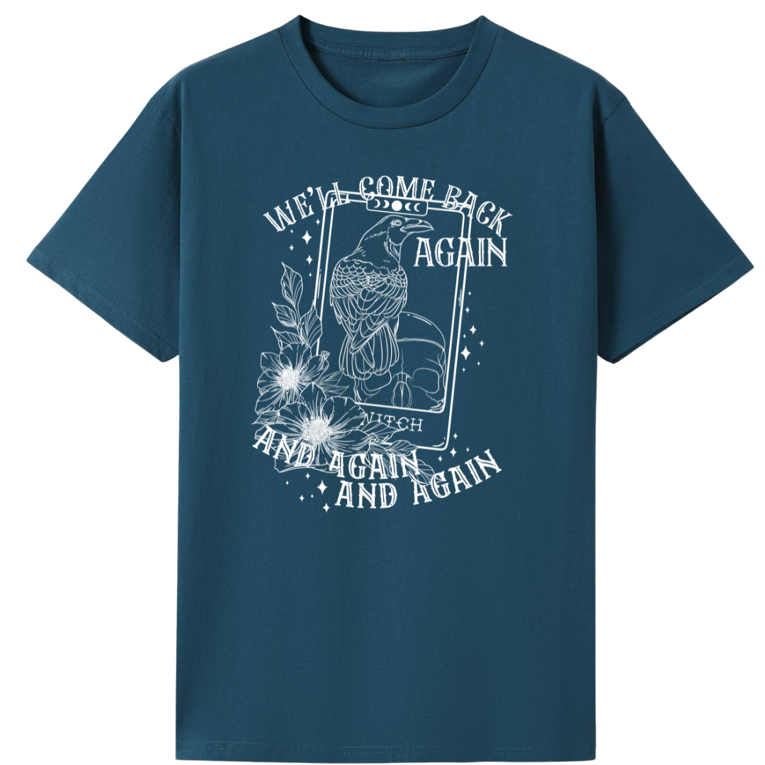 A teal oversized tee with the We'll Come Back Again graphic printed large on the front, a crow on a tarot card framed by flowers.